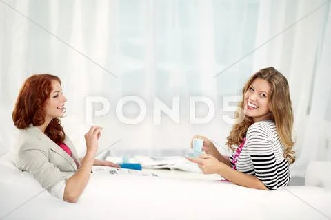 Two young women sitting on sofa, looking at camera and smiling Stock Photos