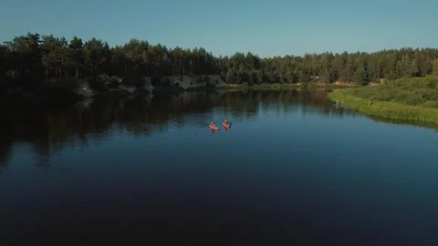 Two young women surf down river on surfboards steering paddle from birds eye 動画素材 318299942