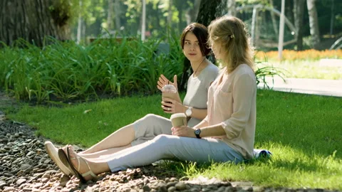 Two young women talking, drinking hot coffee and cold juice in a summer park. 4K 库存影片 87725329
