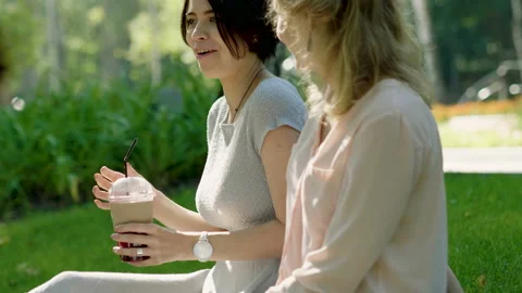 Two young women talking, drinking hot coffee and cold juice in a summer park. 4K Stock-Footage 87725815