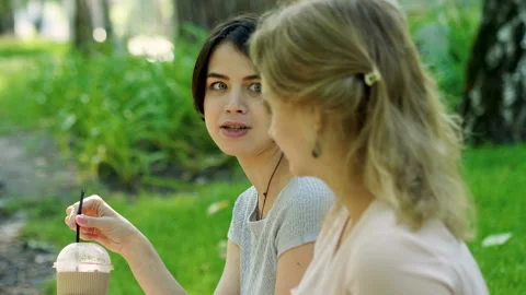 Two young women talking, drinking hot coffee and cold juice in a summer park. 4K Vidéo 87837408