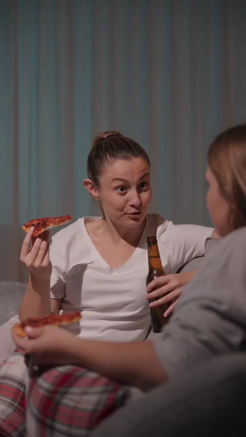 Two young women talking on sofa while eating pizza Stock Footage 241312652