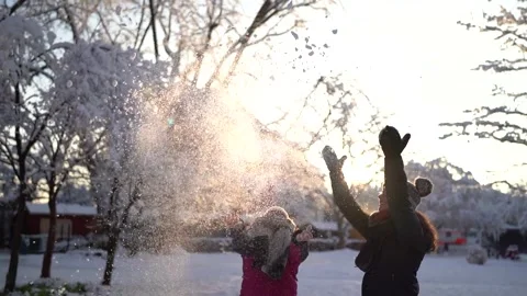 Two young women throwing snow in the air in a sunlit park in slow motion Stock Footage 258371019