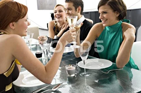 Two Young Women Toasting With Champagne At A Dinner Party