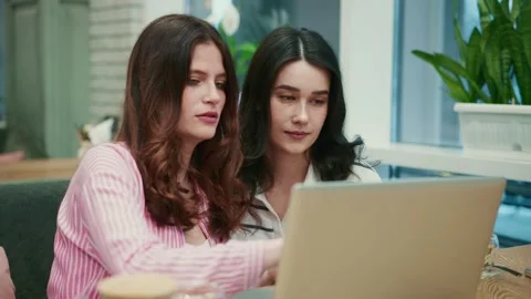 Two young women using a laptop in a cafe Stock Footage 306588057