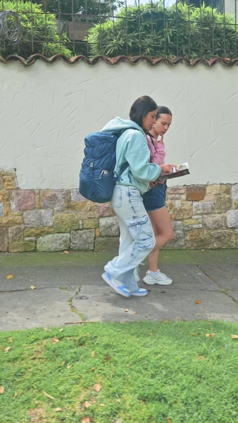 Two Young Women Walking With Backpack and Map Along Residential Street. 動画素材 333646845