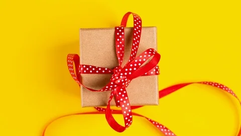 Tying red ribbon bow on craft paper gift box, slow motion. Holiday concept. Stock Footage 119335232