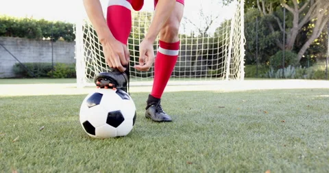 Tying soccer cleats, player preparing for game on field with soccer ball Stock Footage 297927400