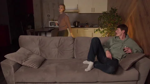 A typical family evening, a guy invites a girl to sit with him on the couch and Stock Footage 145069225
