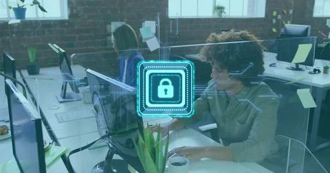 Typing curly-haired man using laptop in open plan office, showing security lock Stock Photos