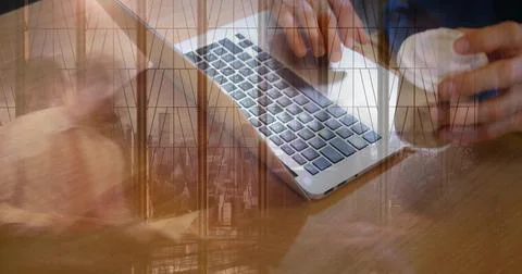 Typing dark-sleeved hands on silver laptop on wooden table, holding coffee cup Stock Photos