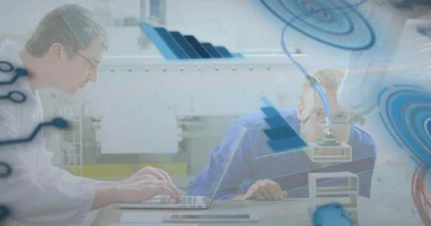 Typing labcoat tech at bench, leaning blue shirt tech checking robot arm and Stock Photos
