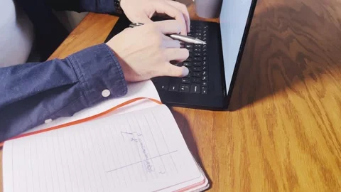 Typing on a laptop and checking notebook at a wooden desk Stock Footage 345150162