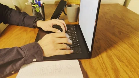 Typing on a laptop and checking notebook at a wooden desk Stock Footage 345150177