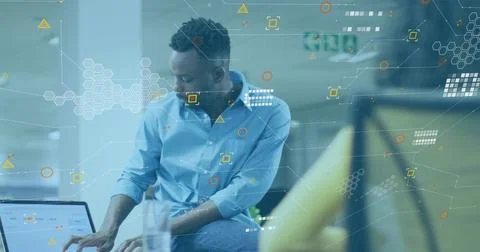 Typing man in blue button-down shirt at open-plan office, laptop HUD, blurred Stock Photos