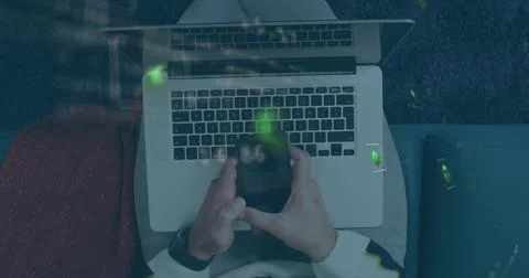 Typing man in light sweater using laptop on lap on sofa, holding smartphone Foto stock