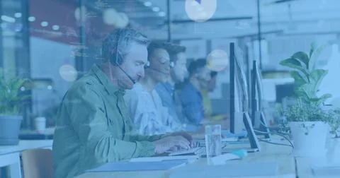Typing mature man in green button-up shirt and headset at open-plan desk with Stock Photos