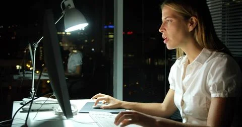 Typing office worker wearing white blouse using computer in office at night, Stock Photos