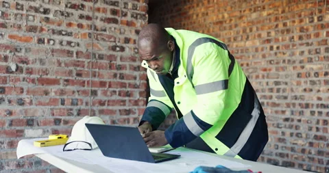 Typing, review or black man with laptop at construction site, renovation Stock Footage 336778718