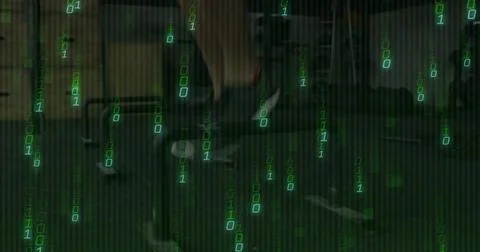 Typing tech wearing dark jacket in dim green office with desk monitors keyboard Foto stock
