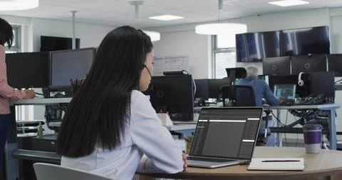Typing woman in white blouse coding on laptop with headset at open office, Stock Photos