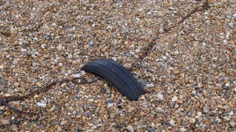 Tyre anchoring rusty chain on shingle beach for use as background Stock Photos