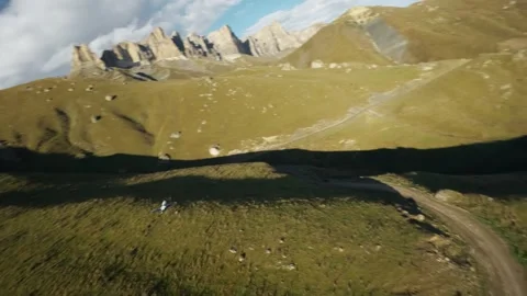 UAV FPV drone flying over green hills with rocky mountains in the background Stock Footage 340956896