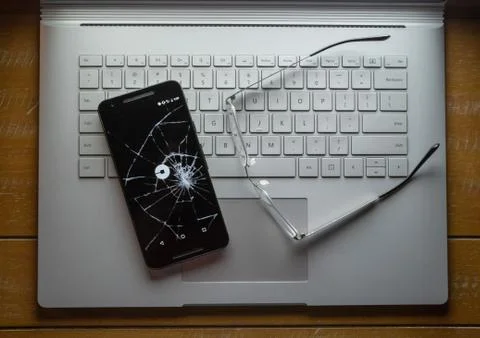 Uber app on a broken cell phone sitting on a laptop next to glasses Stock Photos