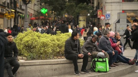 Uber Eats delivery Man sitting relaxing on a Crowded Street of Madrid Stock Footage 105787257