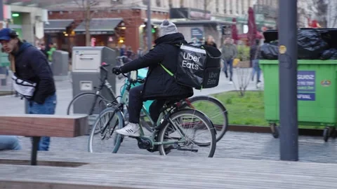 Uber Eats delivery rider driving past two Deliveroo couriers waiting for Stock Footage 171857882