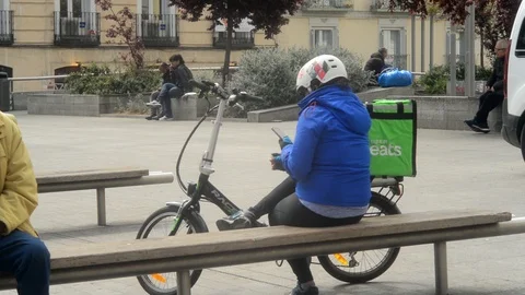 Uber Eats delivery Woman sitting relaxing on a Street of Madrid Stock Footage 105787754