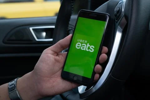 Uber Eats holding smartphone in car. Uber is an American company offering tra Stock Photos
