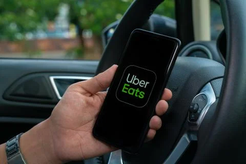 Uber Eats holding smartphone in car. Uber is an American company offering tra Stock Photos