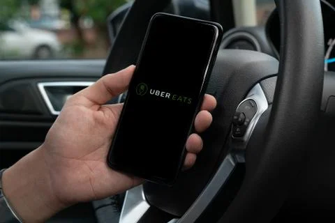 Uber Eats holding smartphone in car. Uber is an American company offering tra Stock Photos