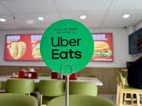Uber Eats "Pick Up Here" sign displayed inside a fast food restaurant. Stock Photos