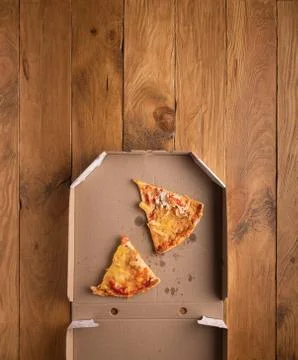 Ugly pizza pieces in pizza box on wooden surface Stock Photos