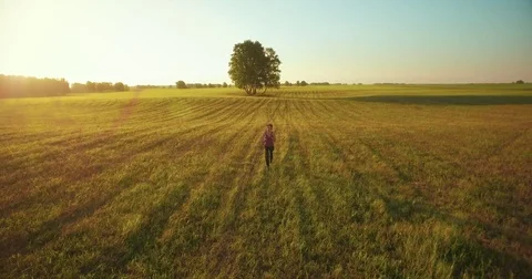 UHD 4K aerial view. Low altitude flight in front of sporty woman at rural field Stock Footage