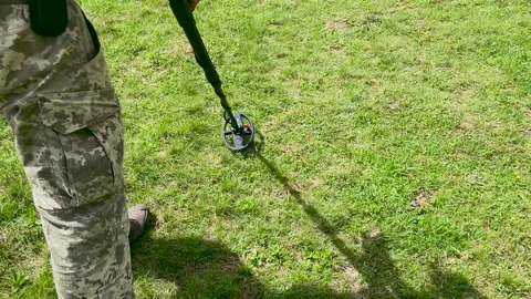 Ukrainian Soldier Using Metal Detector Outdoors for Mine Detection on Grass Stock Footage 246648467