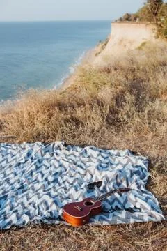 Ukulele and sunglasses lying on blanked on rocky coast Stock Photos