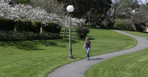 Ultra HD 4K Pan left young happy beautiful blonde woman walking path park spring Stock Footage 32246994