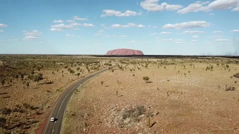 Uluru / Ayers Rock with a car on the road - Aerial Panoramic Drone Shot sun set Video stock 138330430