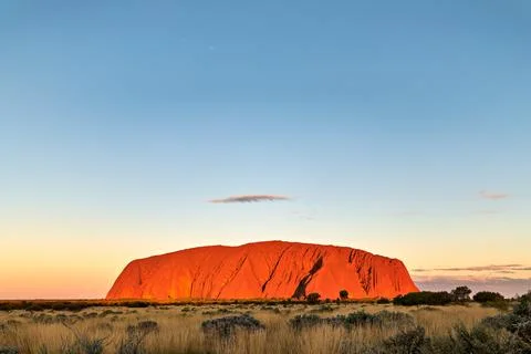 Uluru glows orange at sunset under a clear blue sky. Stock Photos
