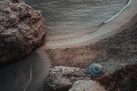 Umbrella in an empty beach with soft waves and big rocks Stock Photos