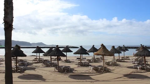 Umbrellas on the beach, a man in the background plays football , couple walk. Stock Footage 99654796
