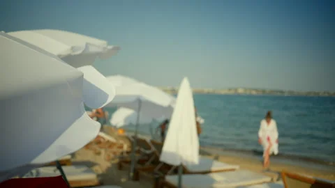 Umbrellas providing shade on a sandy beach, with a person walking in the clear Video stock 343206454