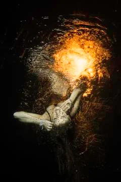 Unconscious girl levitates underwater with fire over the surface Stock Photos