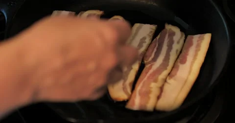 Uncooked bacon being placed into cast iron skillet. Video stock 138332989
