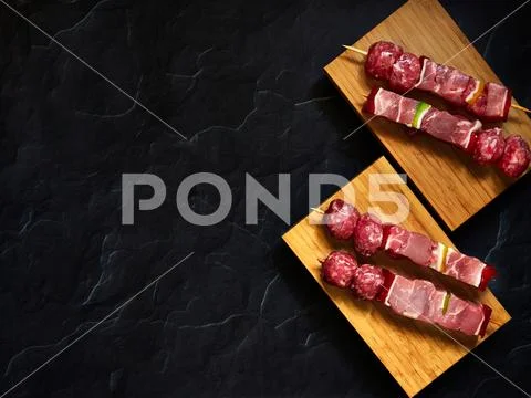 Uncooked beef skewers top down view isolated over a wood plank with a dark ba Stock Photos