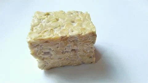 An uncooked block of tempeh showcasing its distinctive texture and light colo Stock Photos