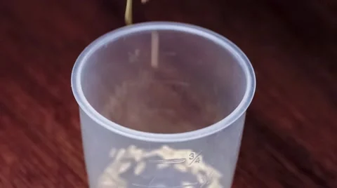Uncooked brown rice grains falling into plastic rice-cooker measuring cup, in Video stock 62799483